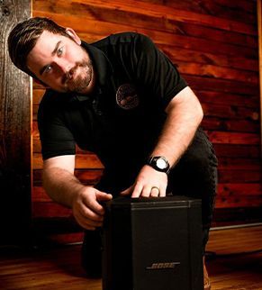 Man kneeling by a black Bose speaker in a wood-paneled room