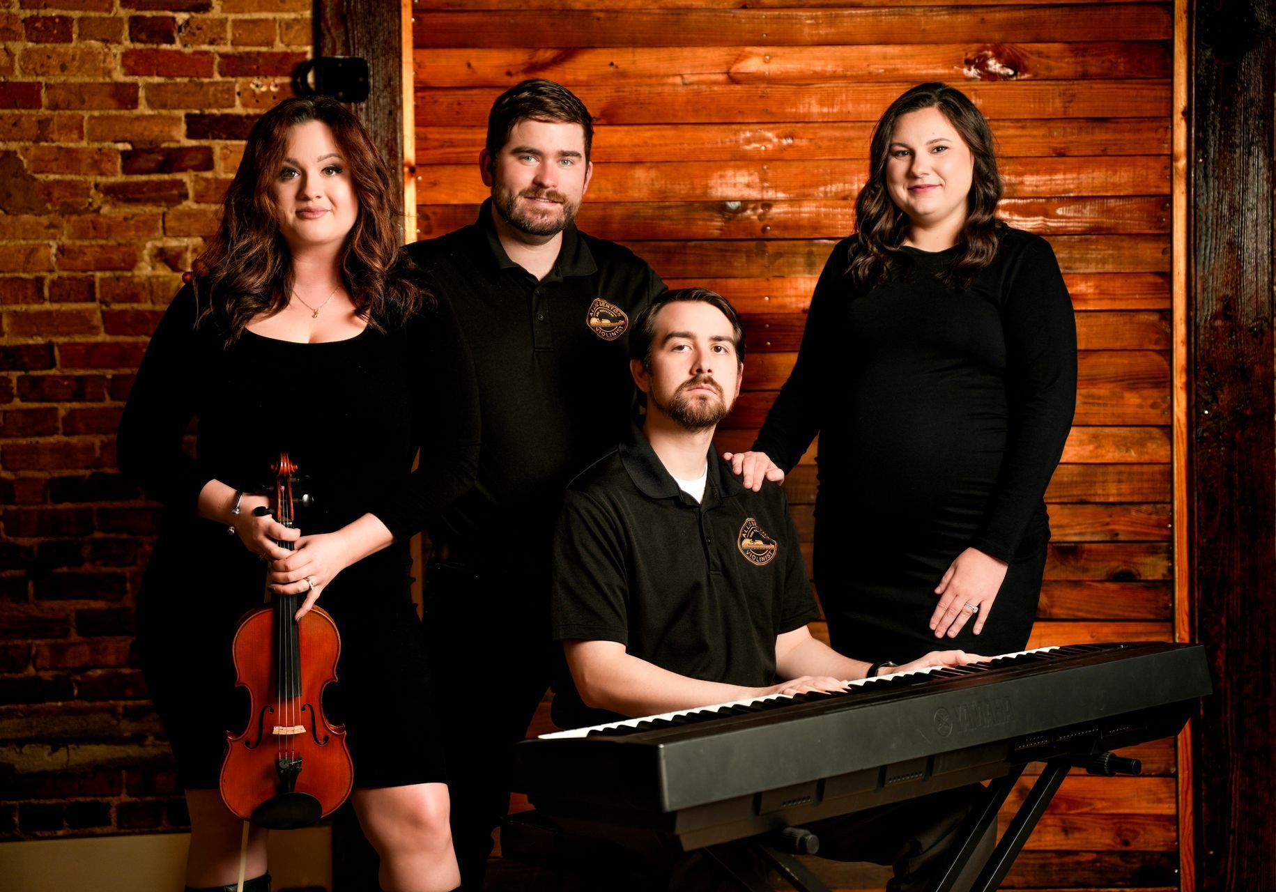 Four musicians posed against a wooden wall, with violin and keyboard in the foreground.