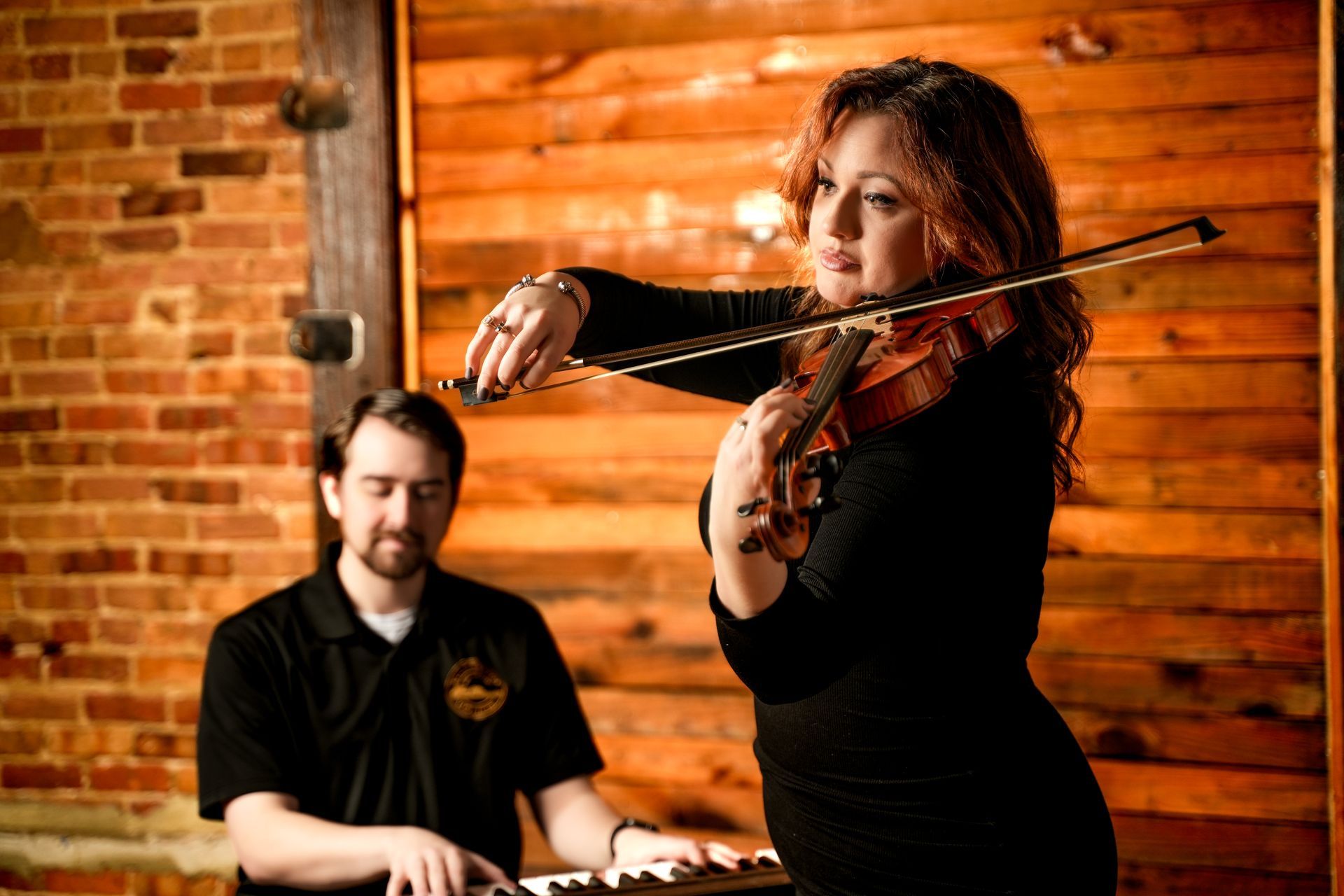 Violinist performing beside a pianist in a warm brick-walled venue