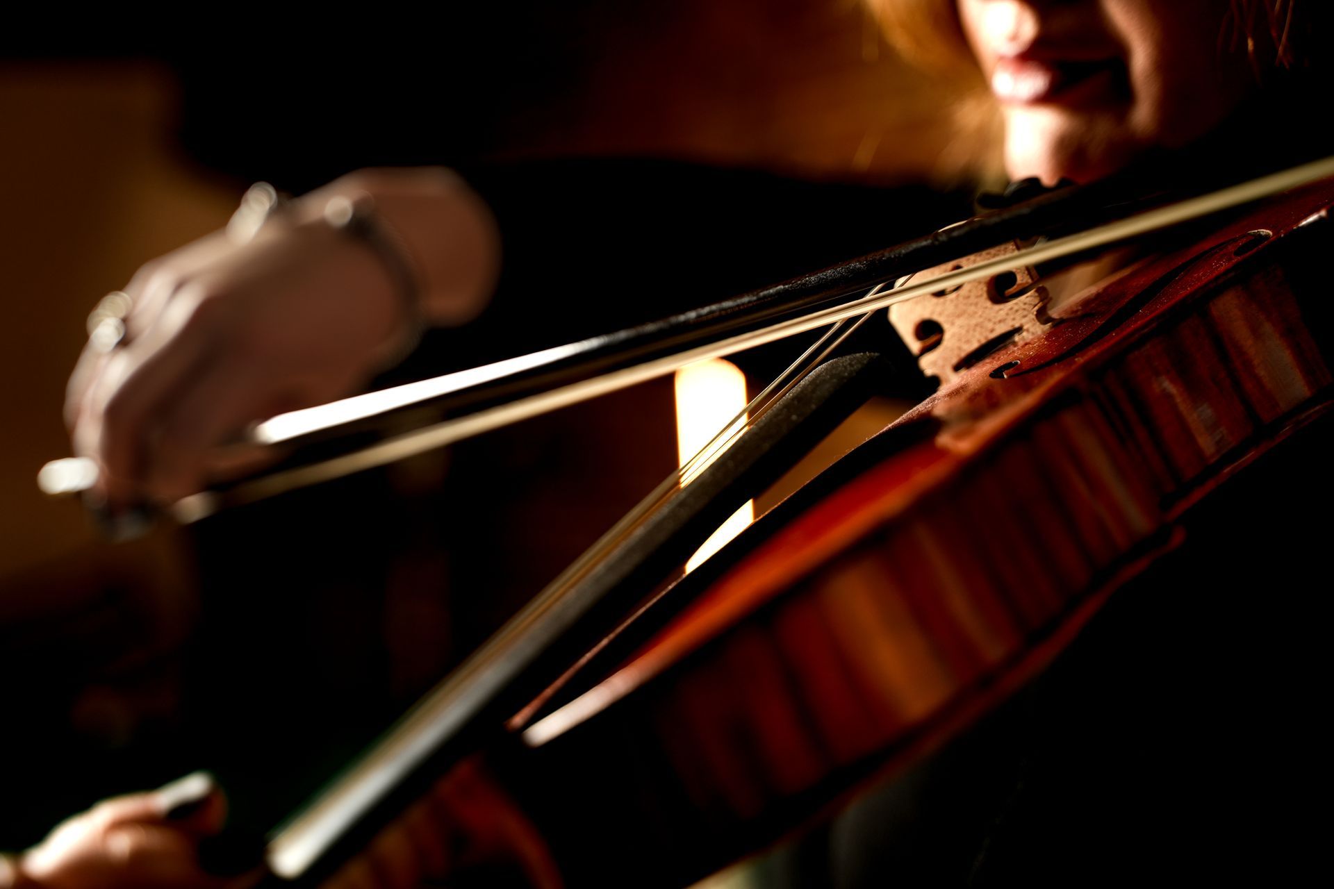 Close-up of a violin being played, with a bow crossing the strings in warm low light