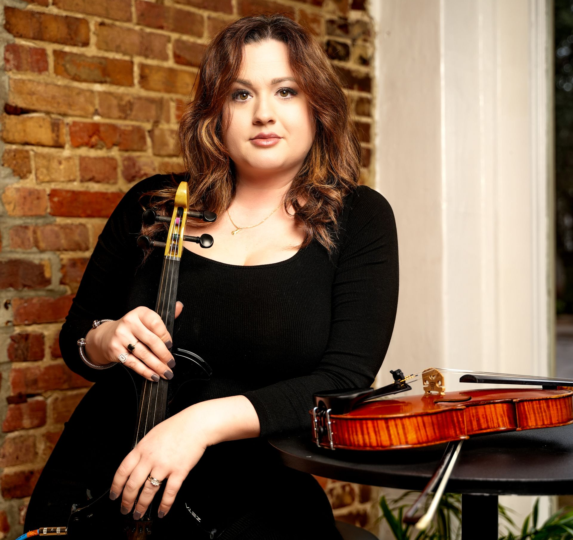 Woman seated with a violin beside her in a brick-walled room