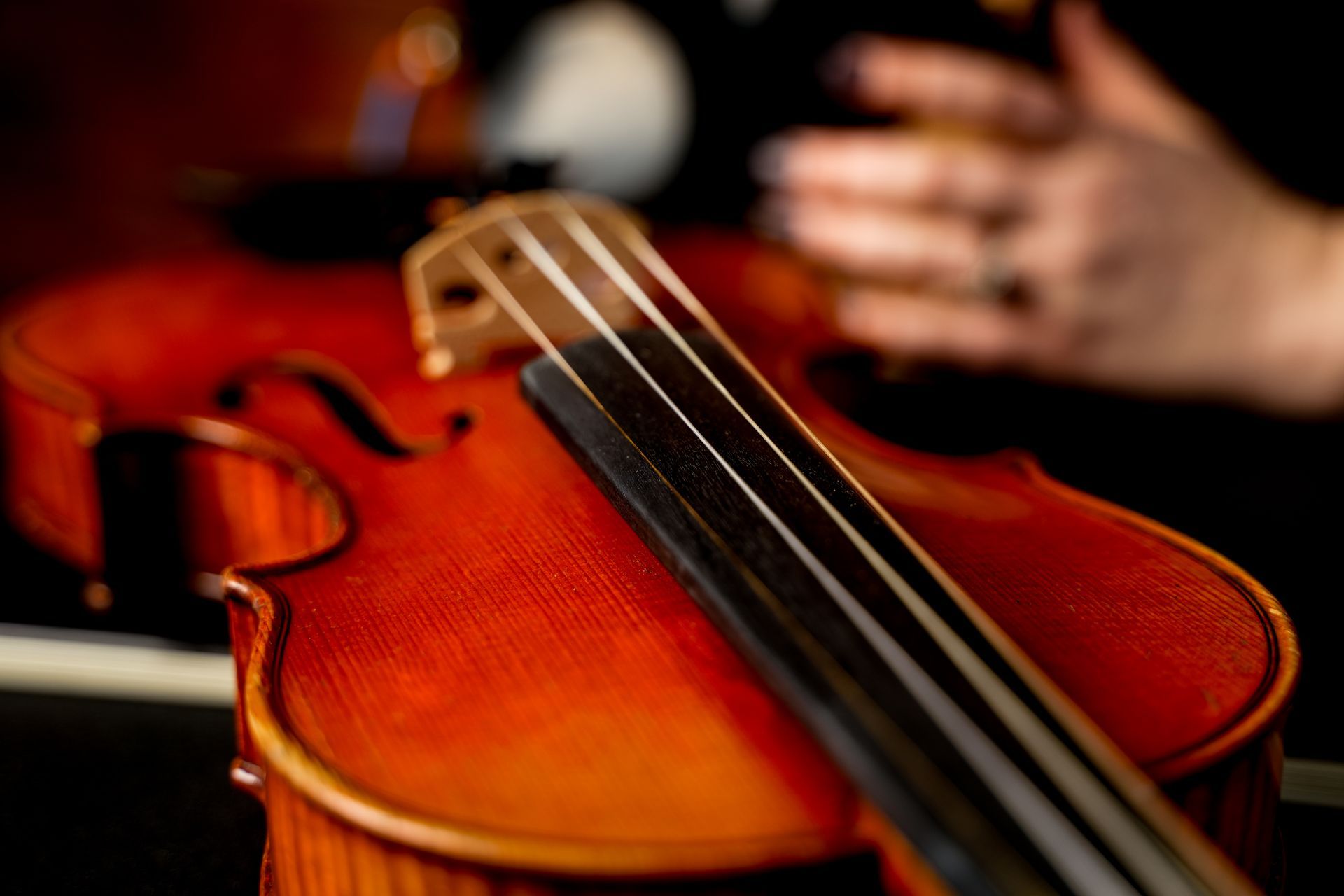 Close-up of a violin being played, with a hand on the strings and warm orange wood