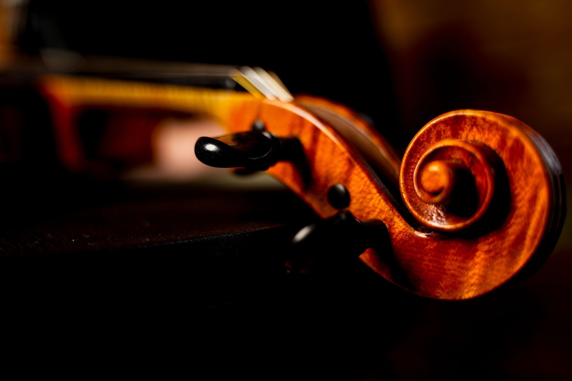 Close-up of a violin scroll and pegbox, warmly lit against a dark background