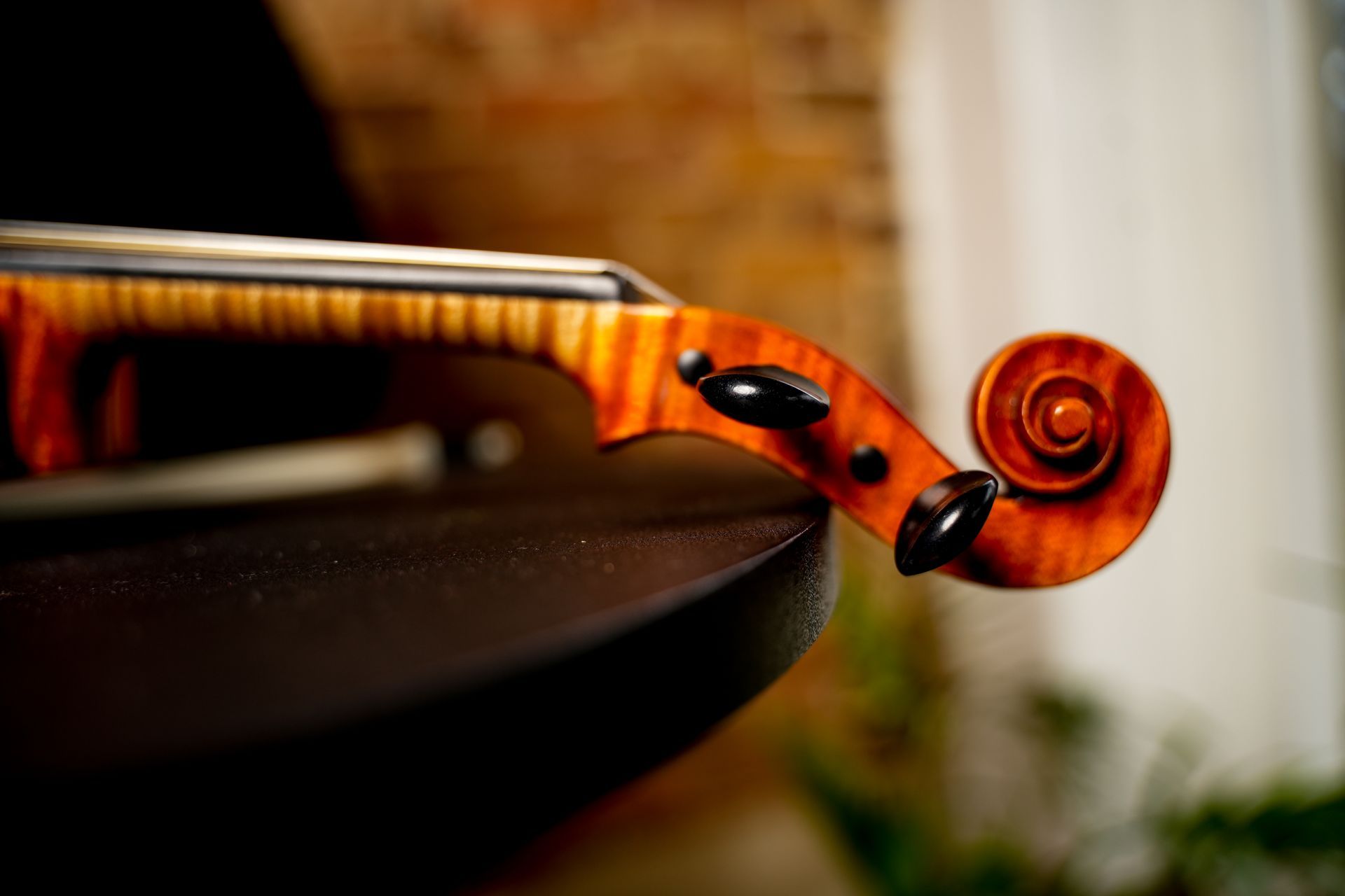 Close-up of a violin scroll and fingerboard with warm wood grain, resting on a dark chair