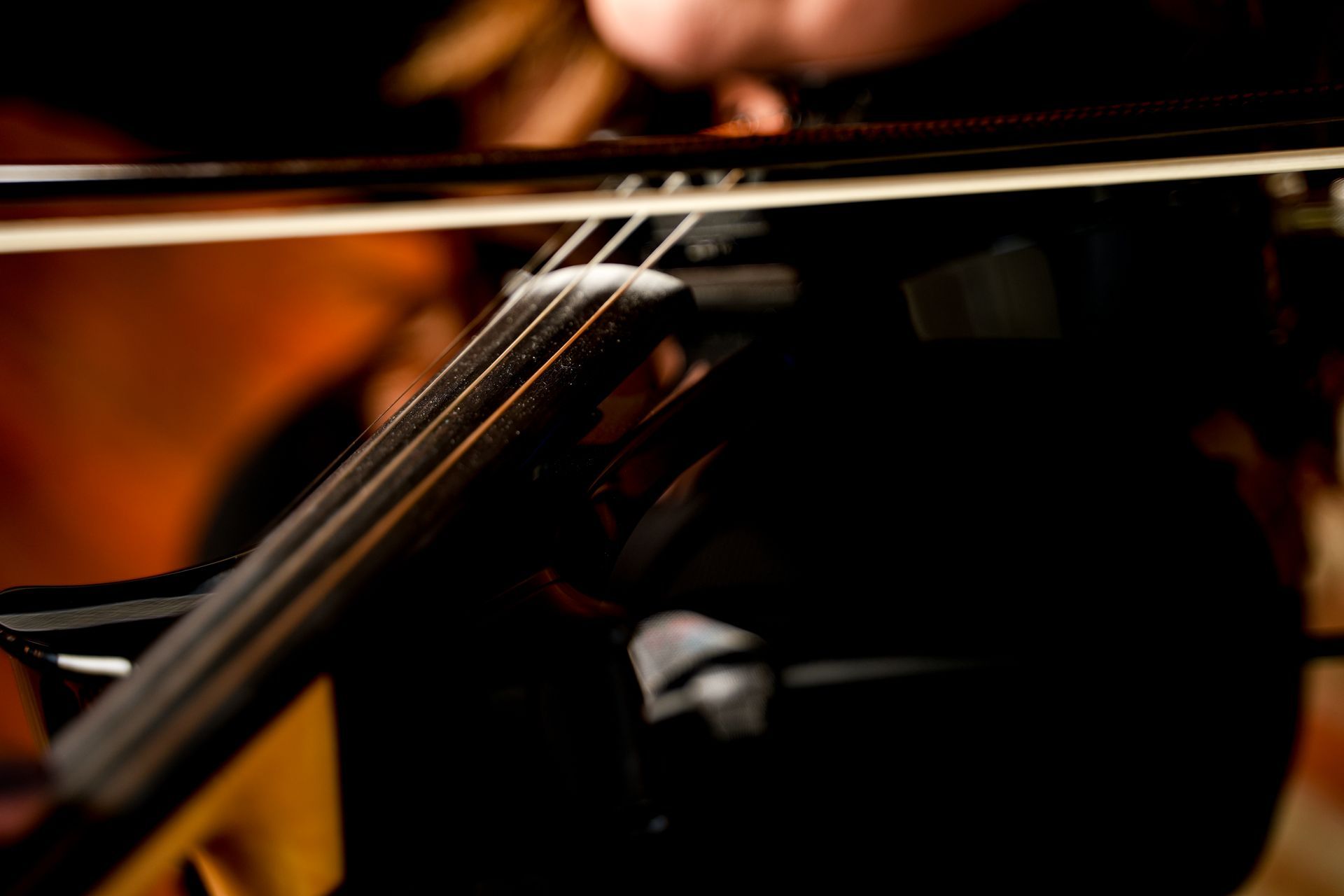 Close-up of a violin being played, with a blurred bow and warm orange stage lighting
