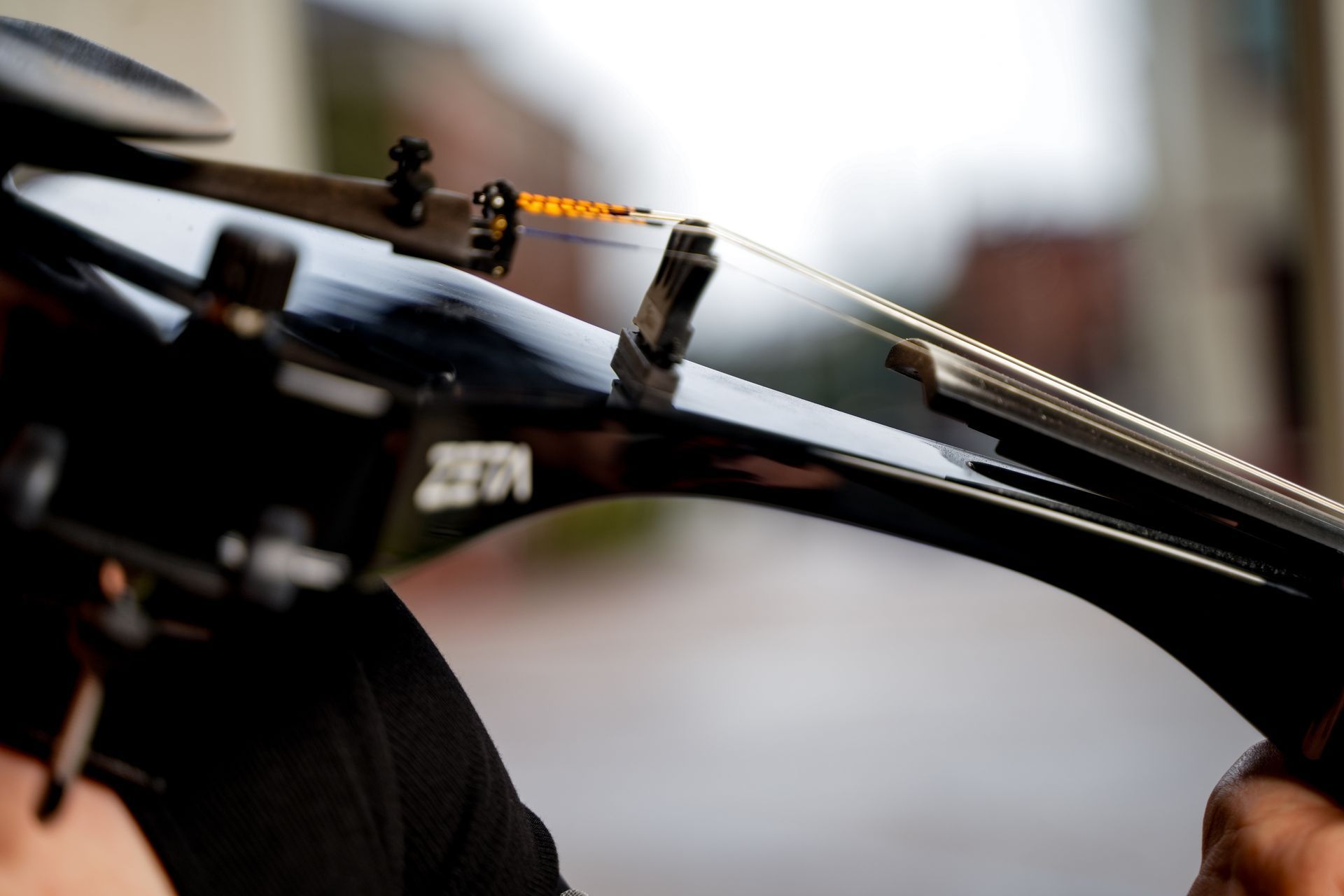 Close-up of a black bike frame and brake cable with a hand adjusting a bolt outdoors