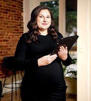 Woman in a black dress holding a clipboard in a warmly lit indoor setting