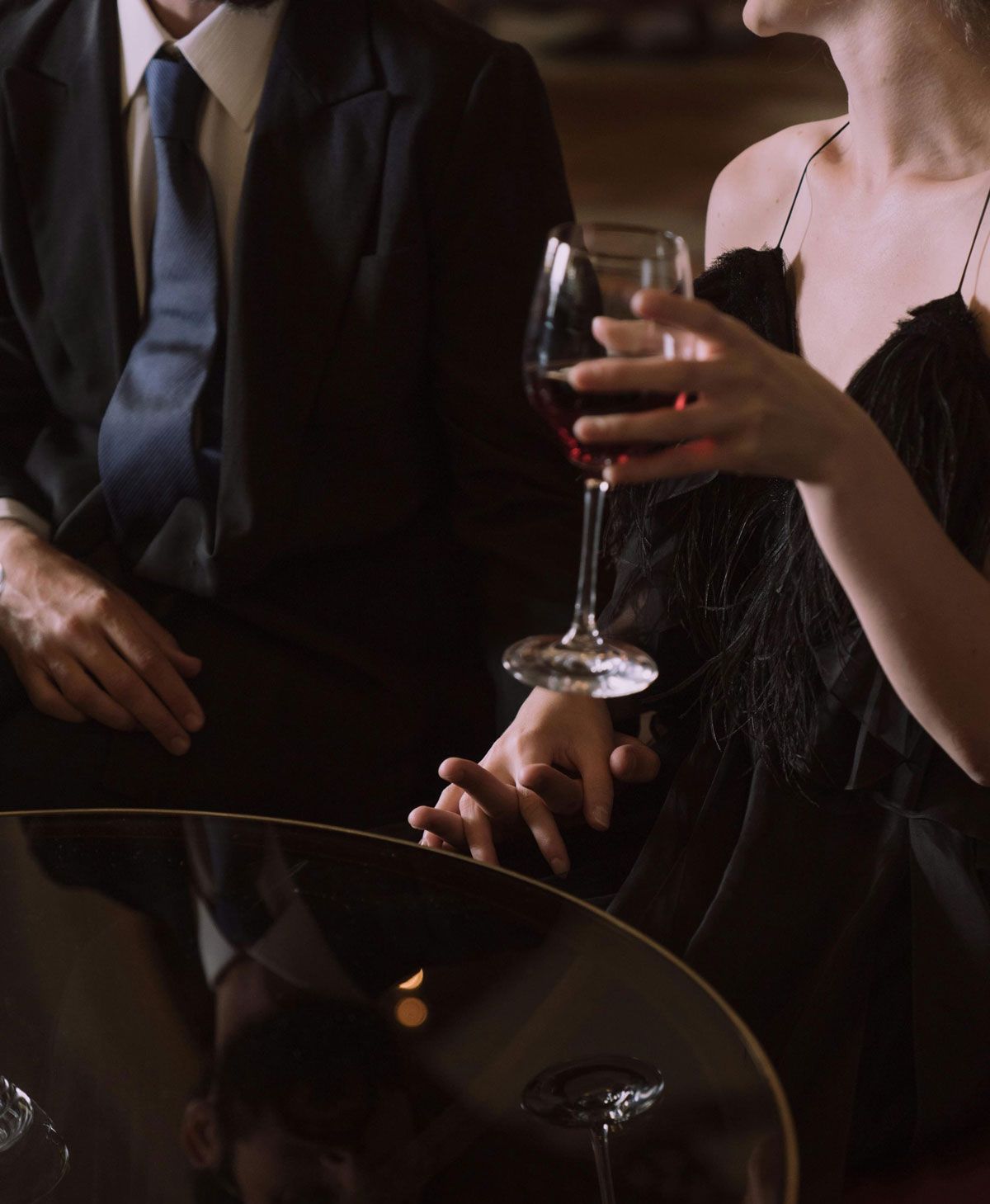 Two people at a dimly lit table, one holding a glass of red wine.