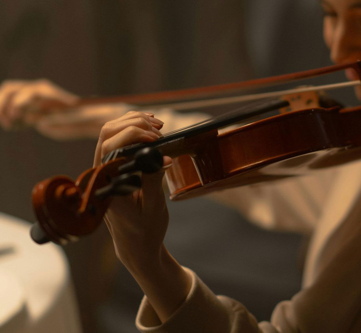 Close-up of a violinist’s hand playing a violin in warm stage lighting