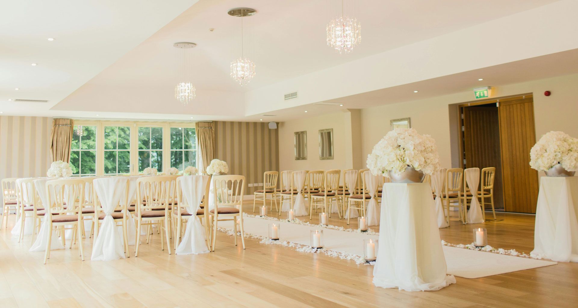 Bright wedding ceremony room with white chairs, floral arrangements, and soft lighting