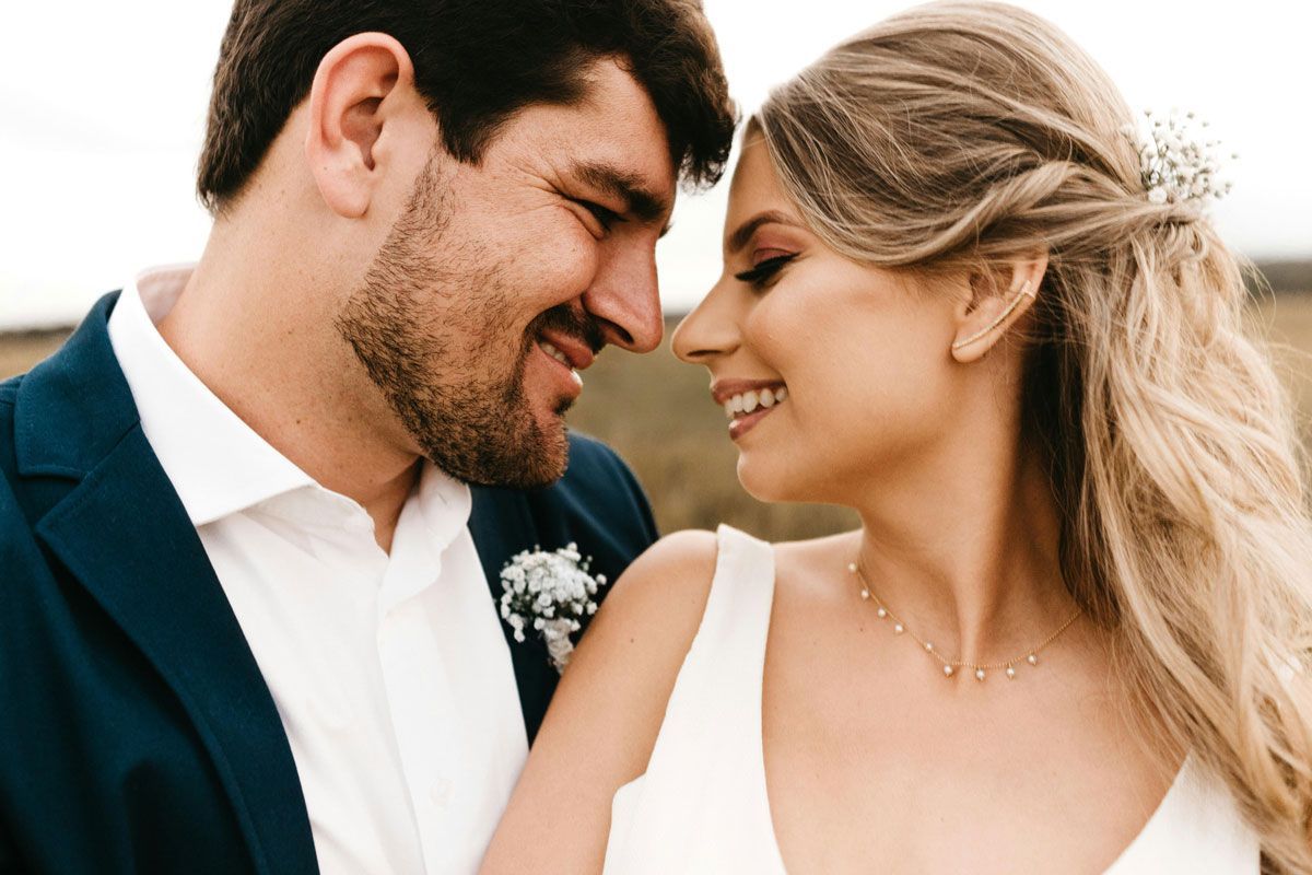 Smiling couple in formal attire touching foreheads outdoors at a wedding