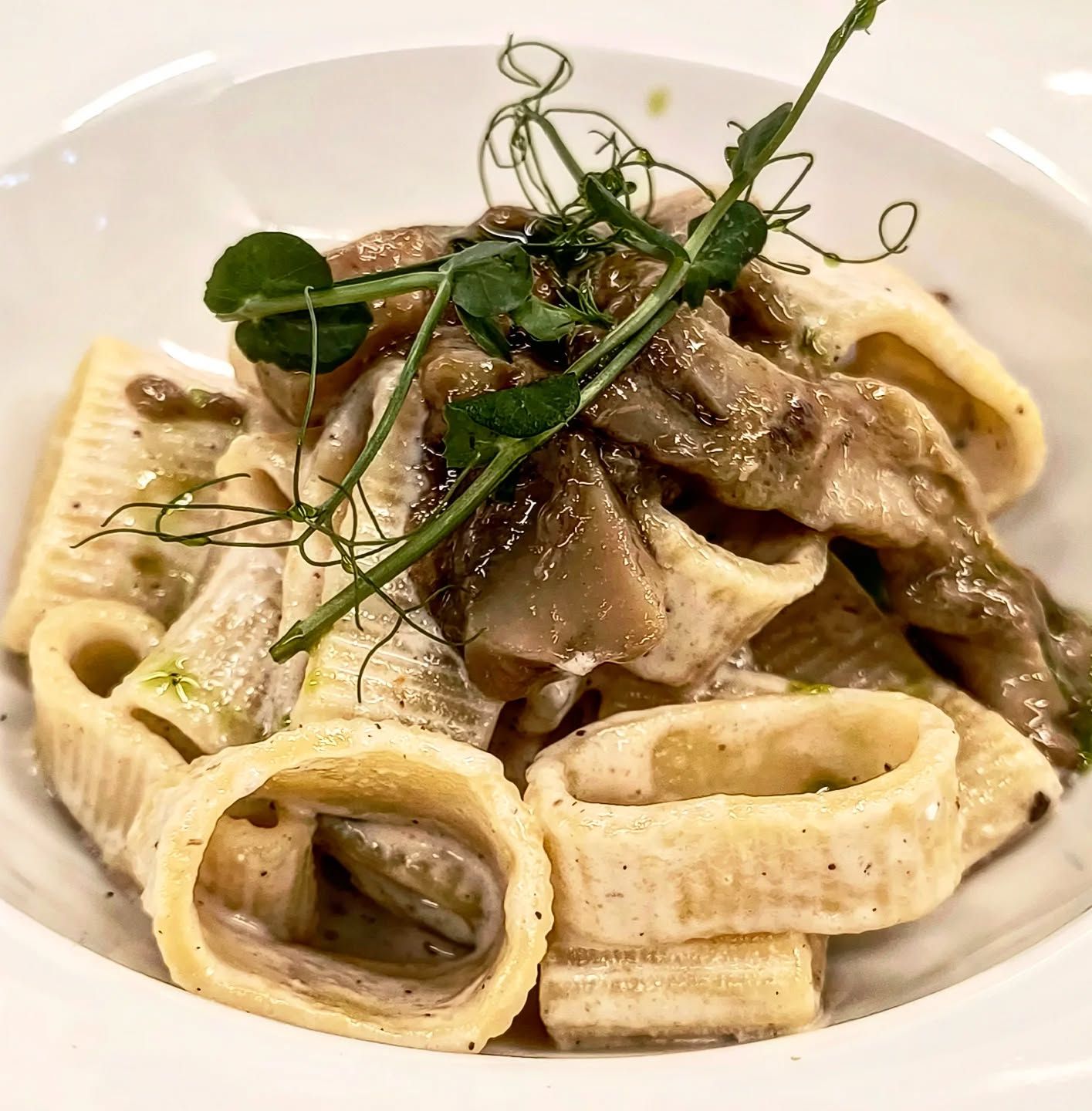 Pasta al ragù in una ciotola bianca su una tavola apparecchiata con posate rosse.