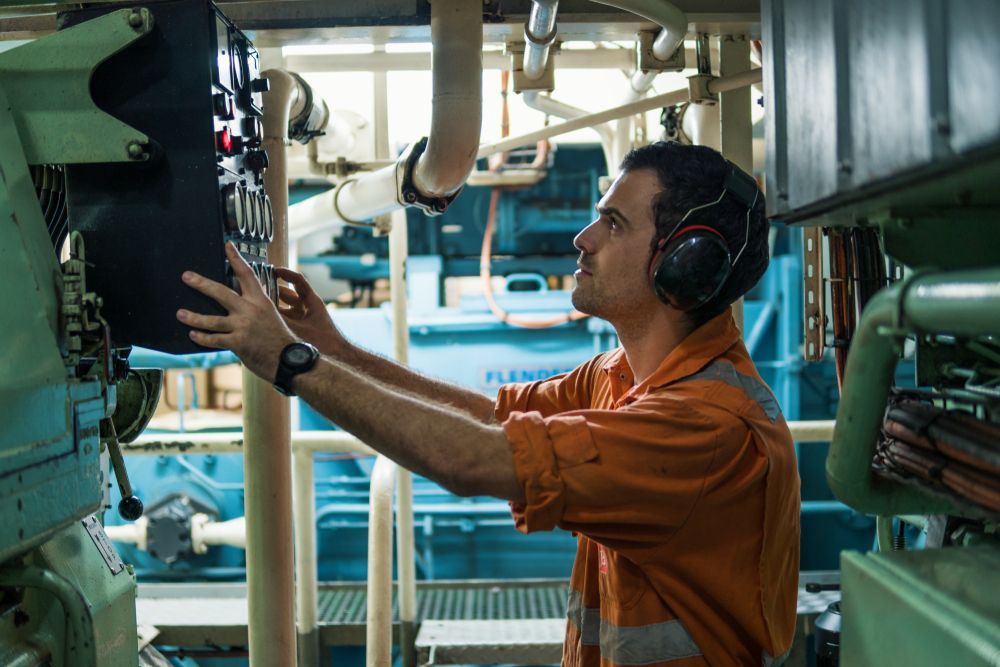 A Man is holding onto a marine engine with earphones on — ElectroMech Machine in Woolner, NT