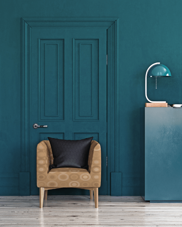 Room with rich green blue wall paint, chair and lamp. 