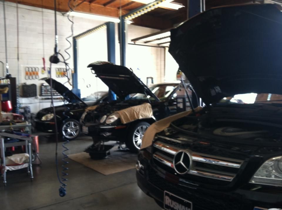 Three cars with open hoods in a garage, lights, tools visible.