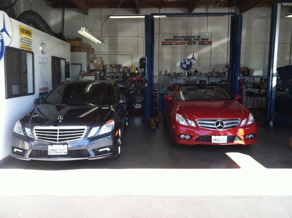 Two Mercedes-Benz cars inside a repair shop; a black sedan and a red convertible.