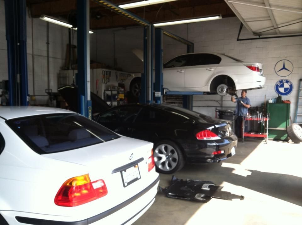 Interior of a car repair shop with several BMWs; a mechanic works on a car lifted on a hoist.