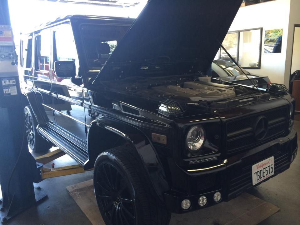 Black Mercedes-Benz G-Wagon SUV with the hood up, in a garage.