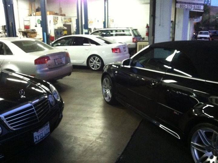Cars inside a repair shop. A black convertible, silver and white sedans, and a white wagon are visible.