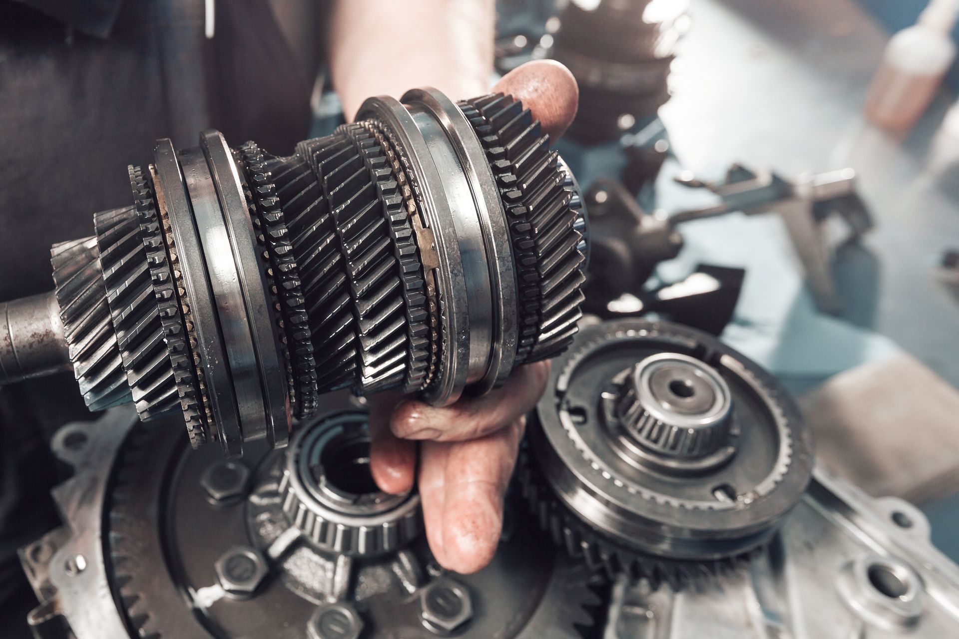 A person holding a gear assembly; car parts on a table.