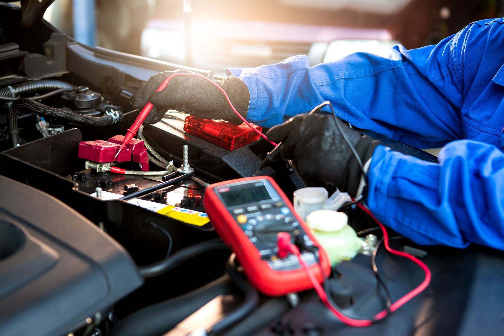 Mechanic using a multimeter to test a car battery in an engine bay.
