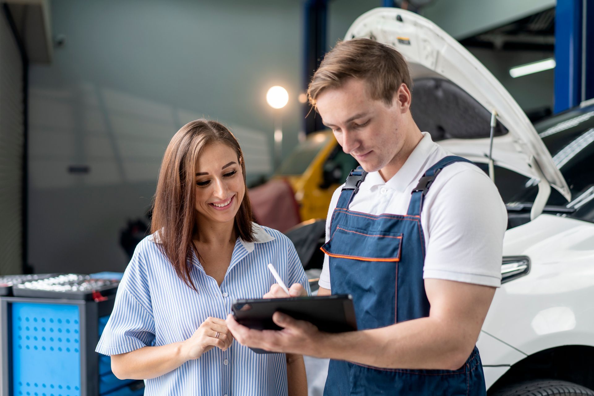 Mechanic showing a woman a tablet in a garage, signing paperwork.
