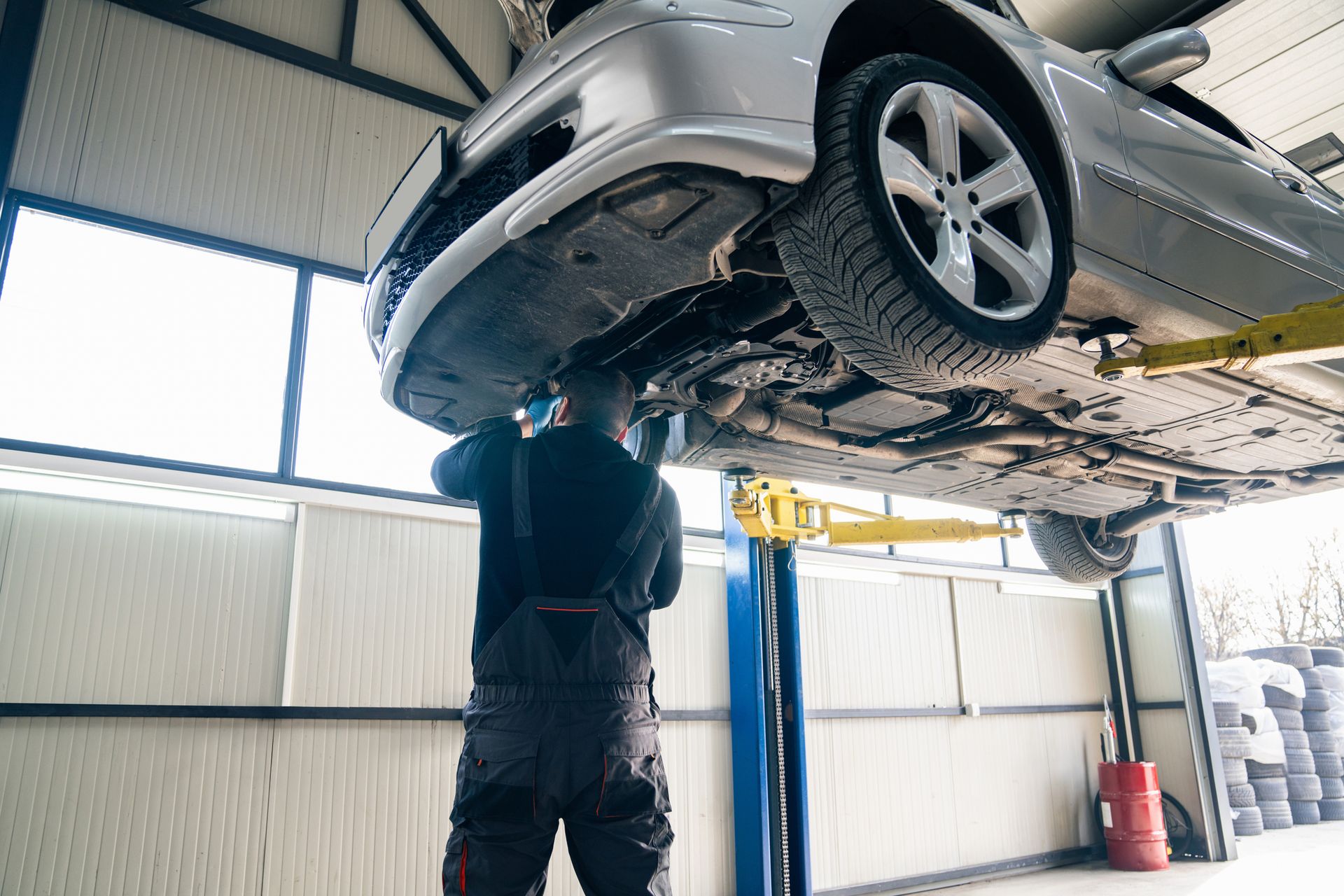Mechanic under a silver car lifted on a hoist in a garage.