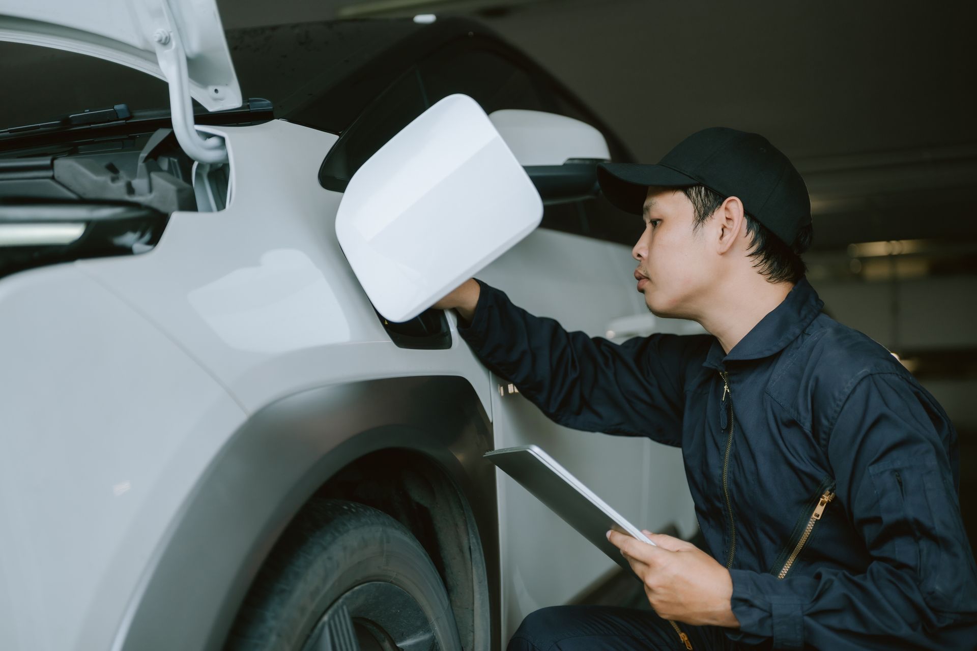 Mechanic inspecting car mirror, holding clipboard, in a garage. Mechanic inspecting car mirror, holding clipboard, in a garage.