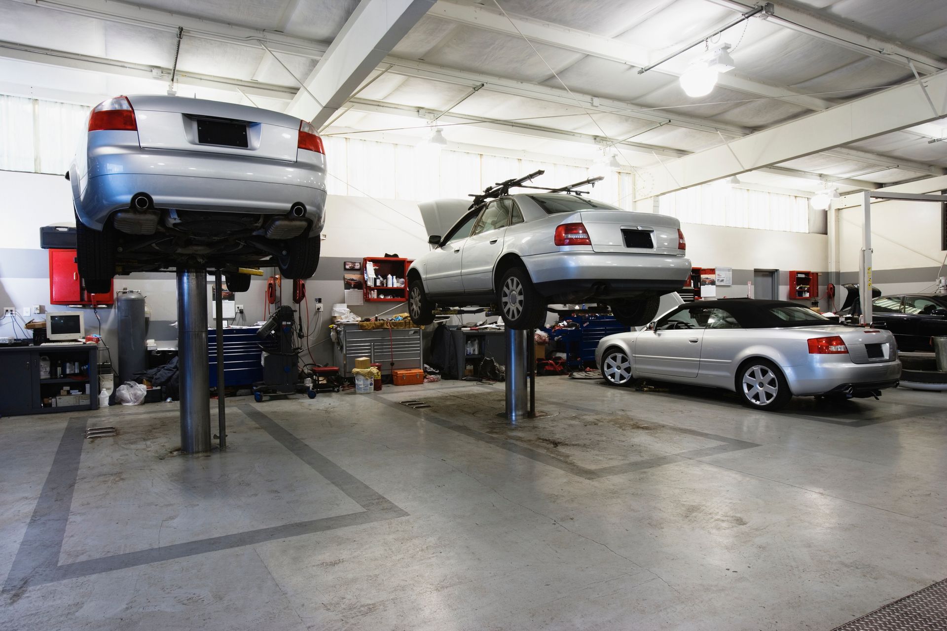 Cars being serviced in a brightly lit auto repair shop; two on lifts, one on the ground.