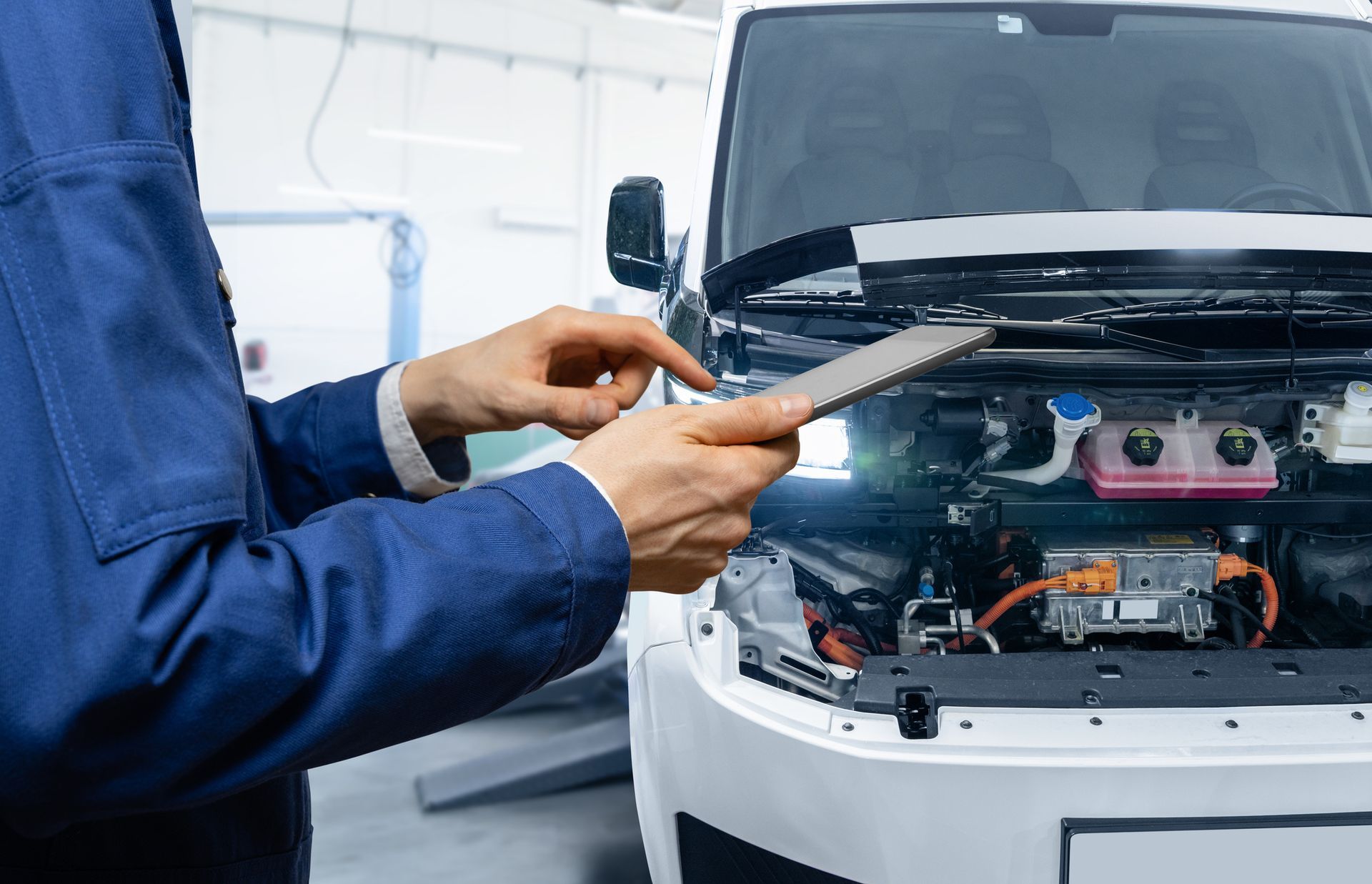 Mechanic examining an EV engine with a tablet in a well-lit auto shop.
