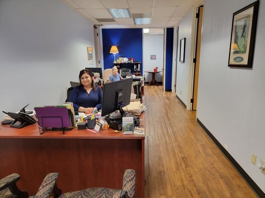 Man in blue shirt, on phone, looking at documents at a desk with a computer and plants.