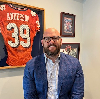 Man in glasses sitting beneath framed red Anderson 39 jersey in an office
