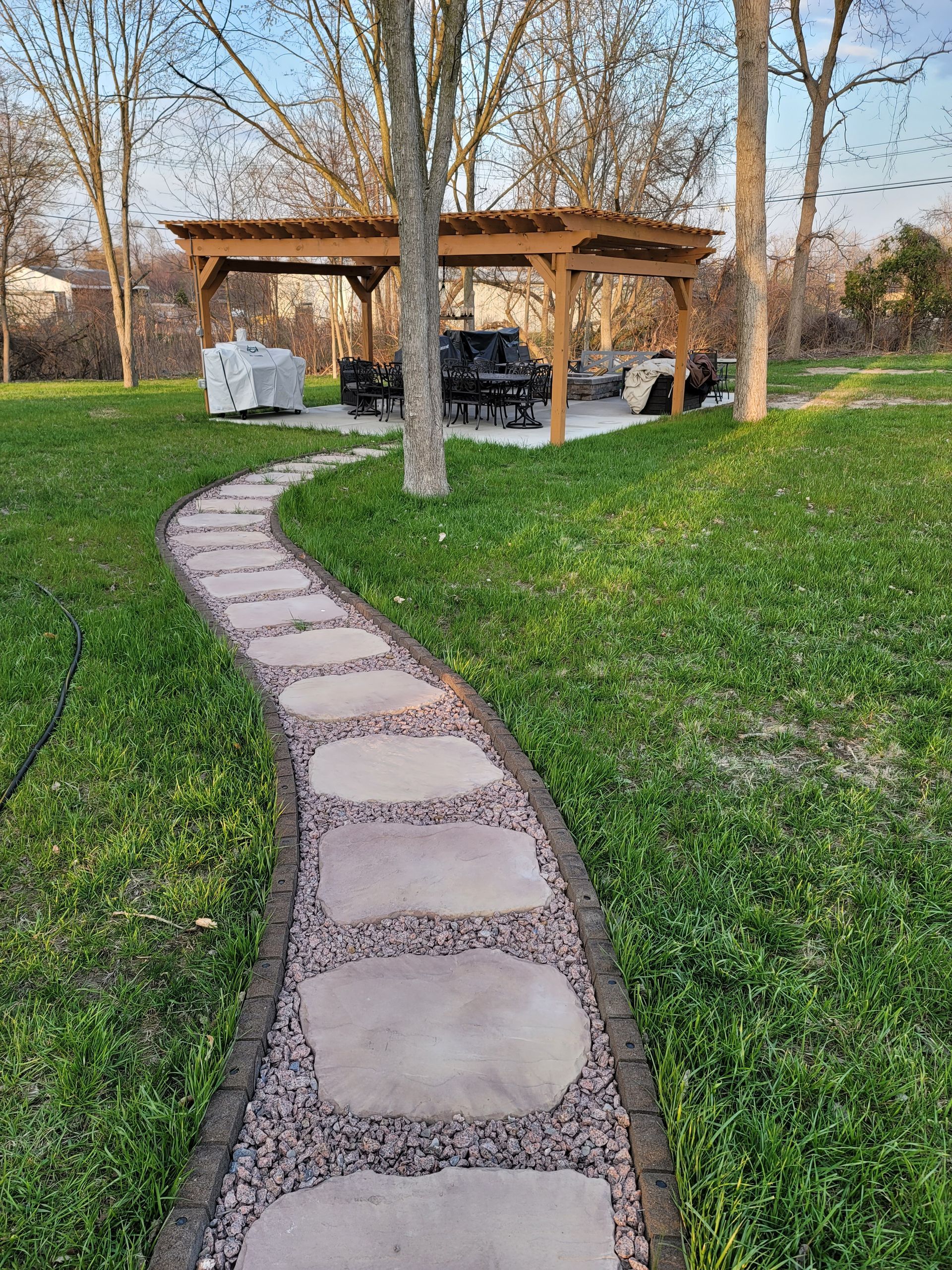 A stone walkway leading to a pergola in the middle of a lush green field.