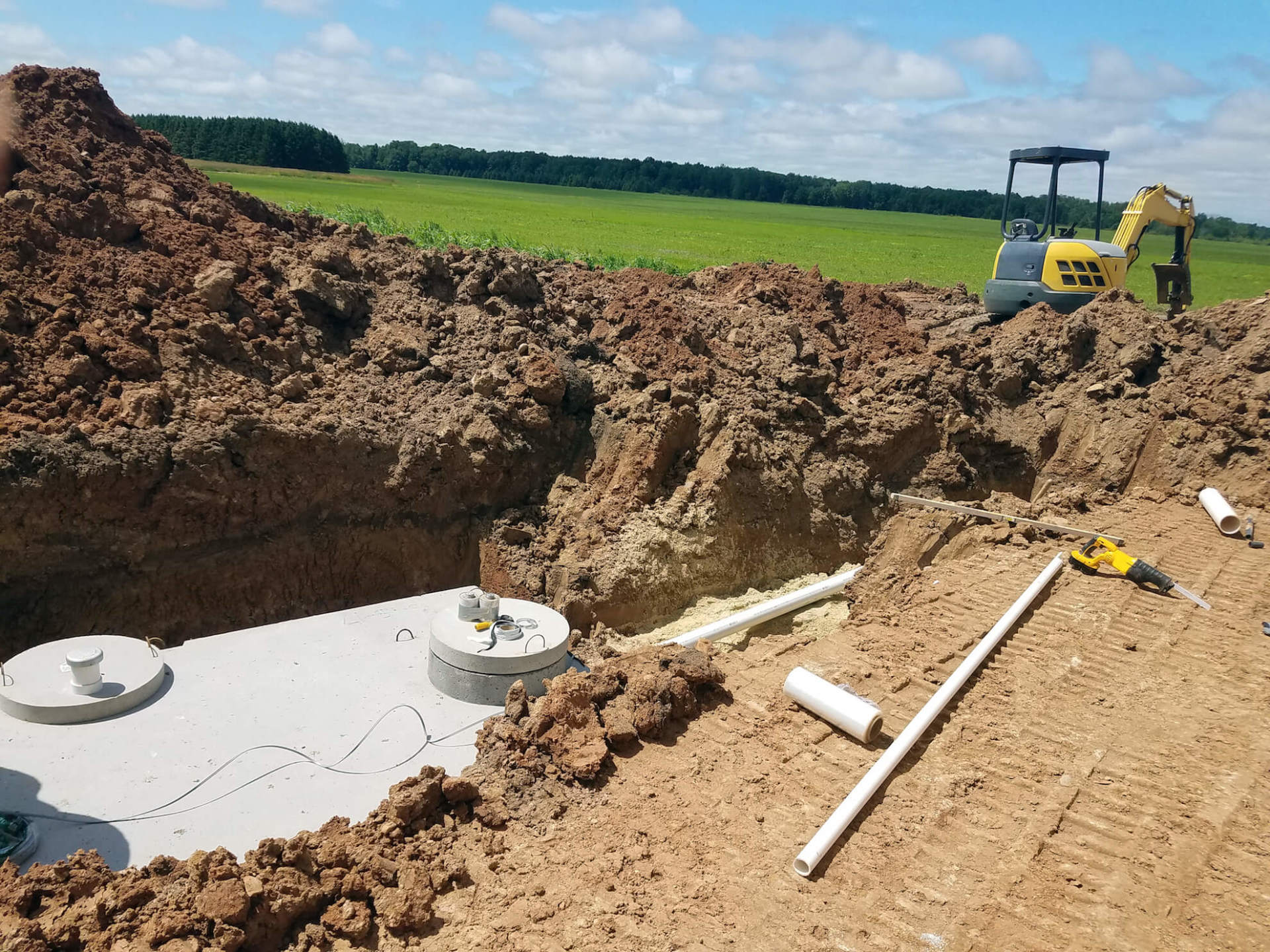 Un grand trou dans le sol avec une excavatrice jaune en arrière-plan.