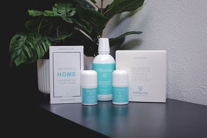 Skincare products in white and teal on a black shelf with a plant, against a white and black wall.
