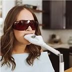 Woman using teeth whitening device, wearing protective glasses.
