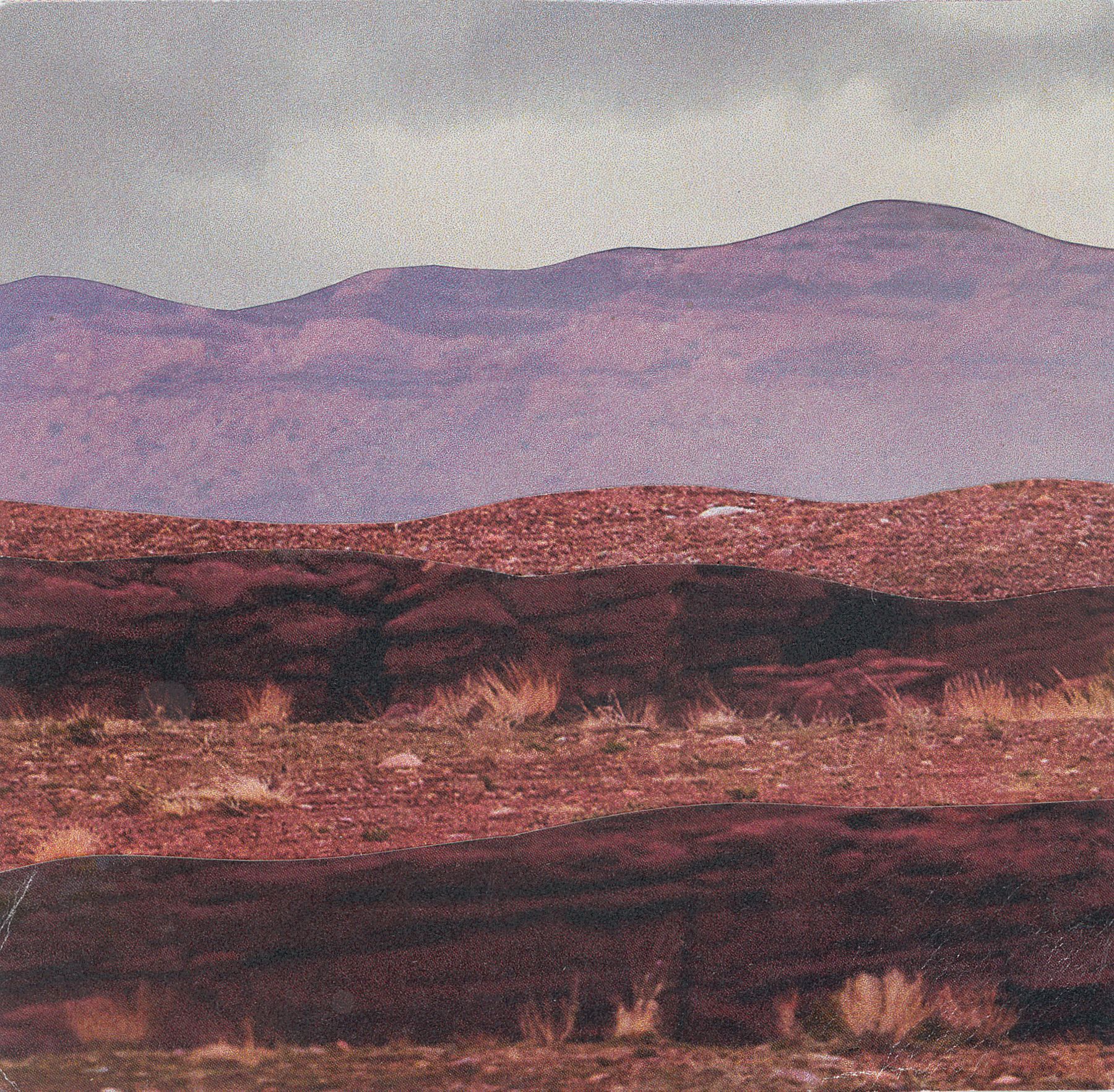 Reddish-brown hills and mountains under a cloudy, gray sky. Some dried grass in foreground.