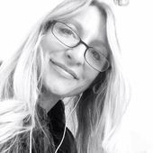 Woman with long blonde hair, glasses, and earphones smiling slightly.