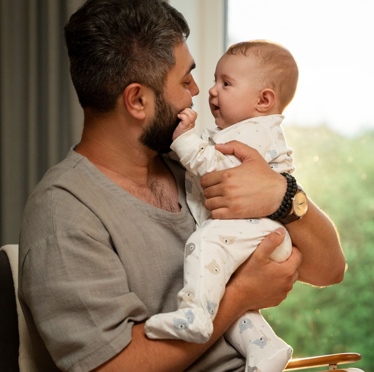 A man is holding a baby in his arms and the baby is looking at the camera.
