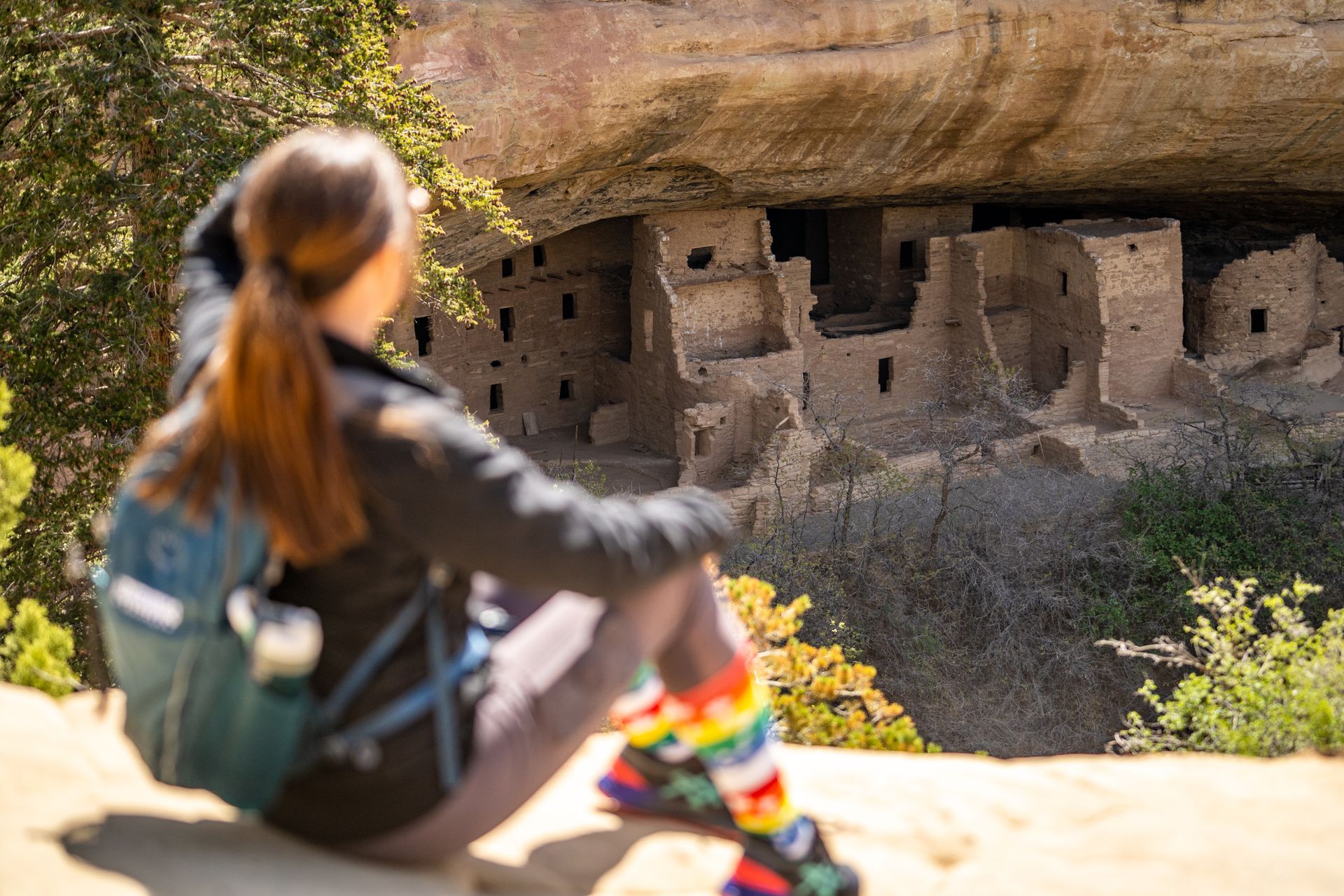 A woman is sitting on a rock looking at a ruined building.