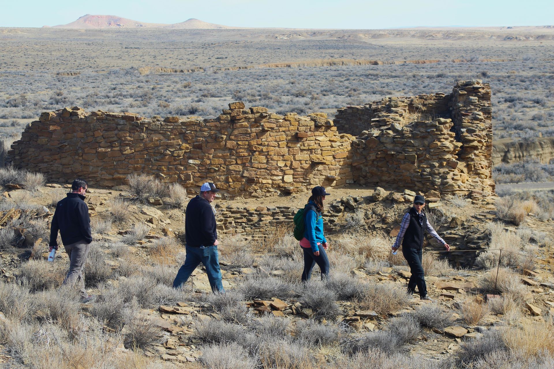 A group of people walking in the desert near a stone wall