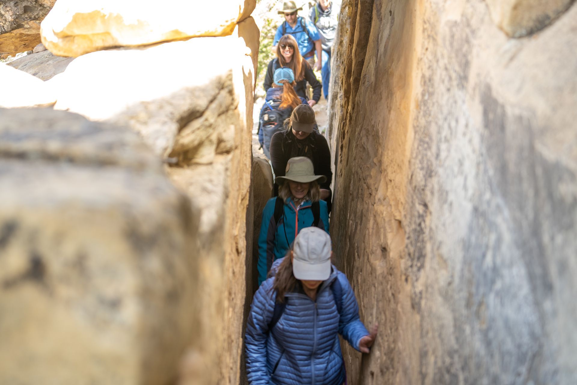 A group of people are walking down a narrow rocky path.