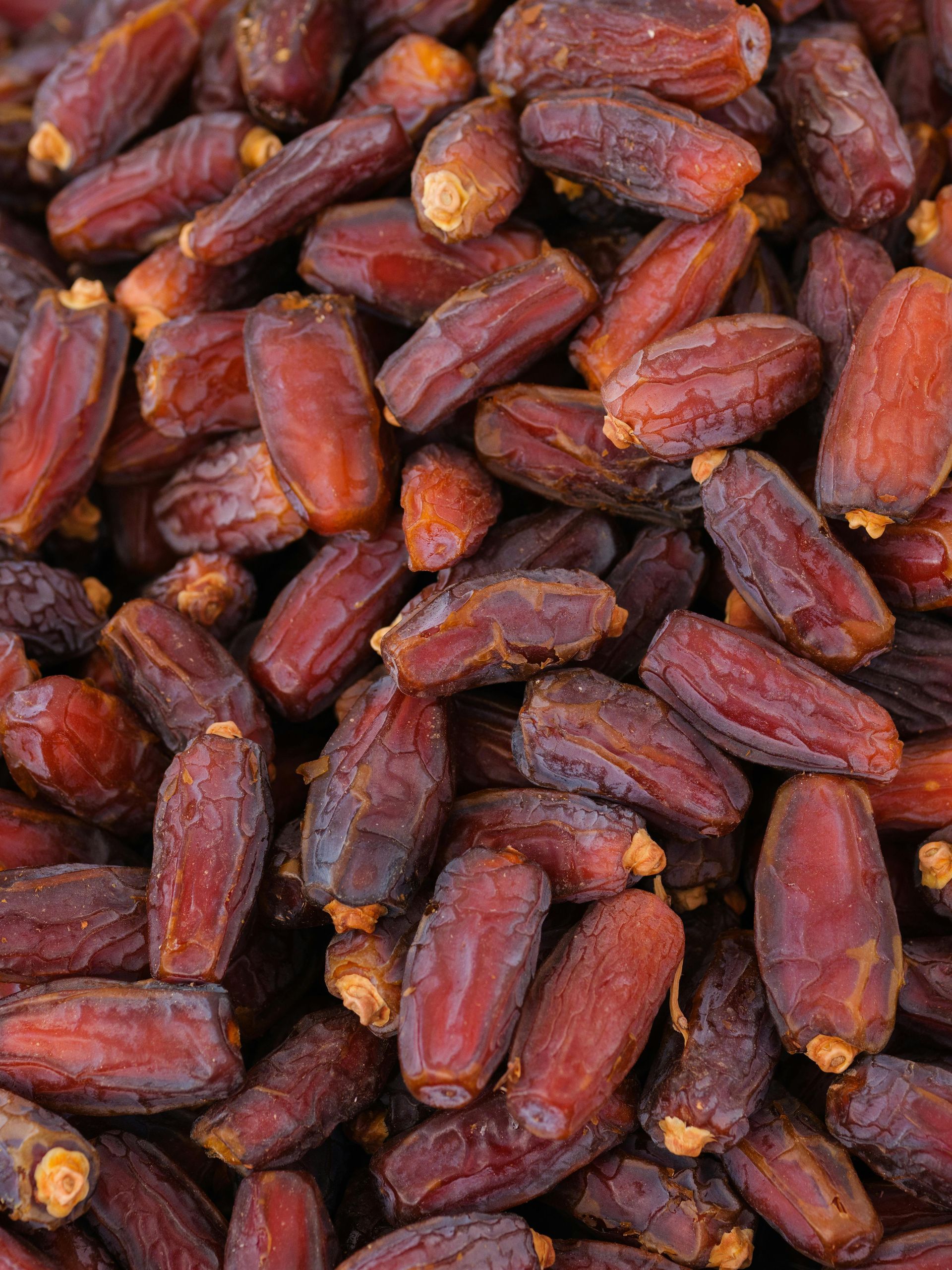 A pile of brownish-red dried dates packed closely together, showing their textured skins and stem ends.