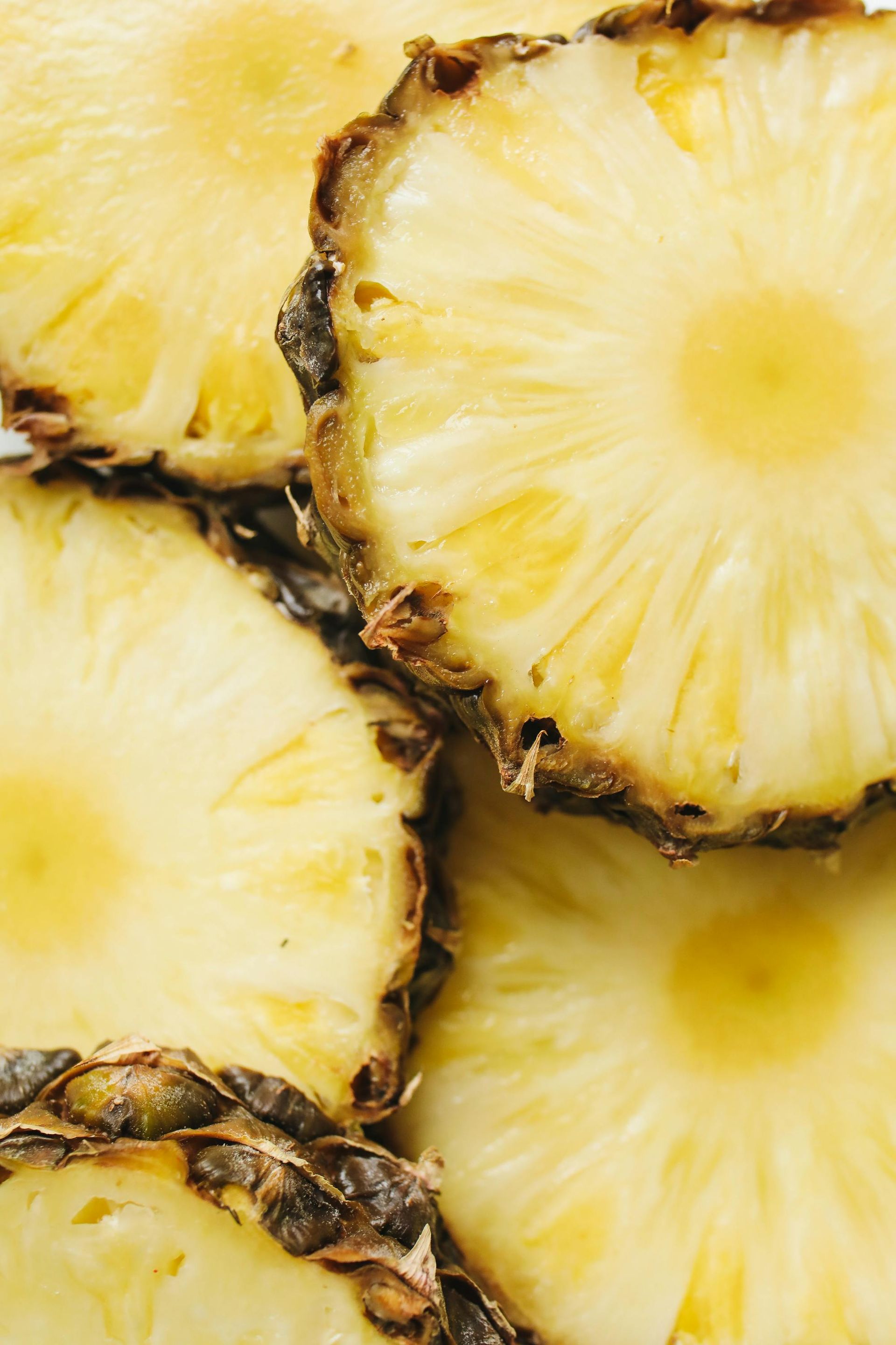A close-up view of multiple fresh pineapple slices featuring yellow, textured fruit flesh and prickly brown rinds.