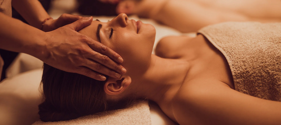 Spa massage with hands gently touching a person’s face on a towel-covered table