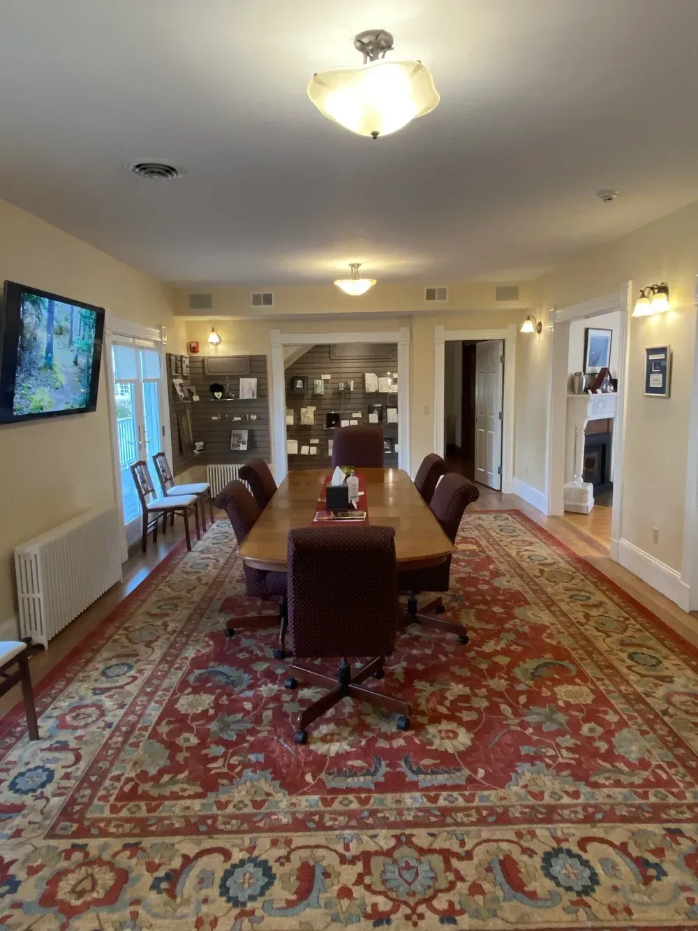 Long dining room with a table, red patterned rug, wall TV, and bright ceiling lights