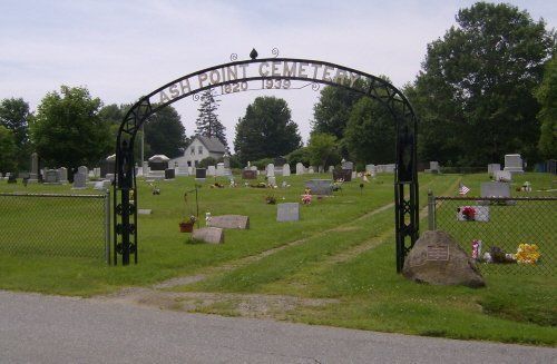 Cemetery entrance with arched gate, gravestones, and a church in the distance