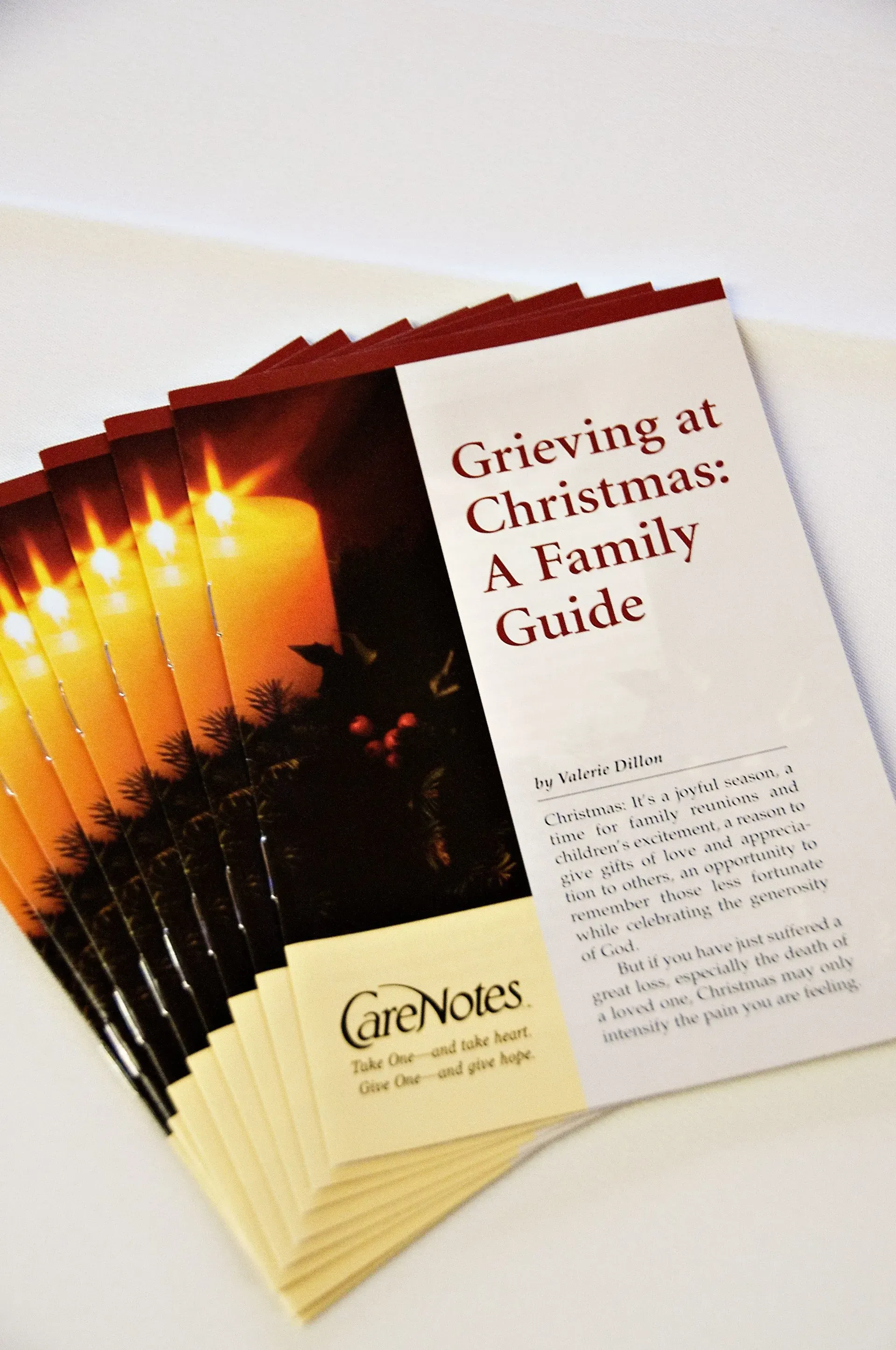 Booklets titled “Grieving at Christmas: A Family Guide” fanned out on a white surface with candlelight cover artwork