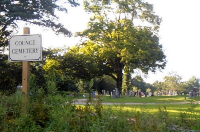 Sign for Council Cemetery beside a sunlit grassy cemetery with trees and gravestones