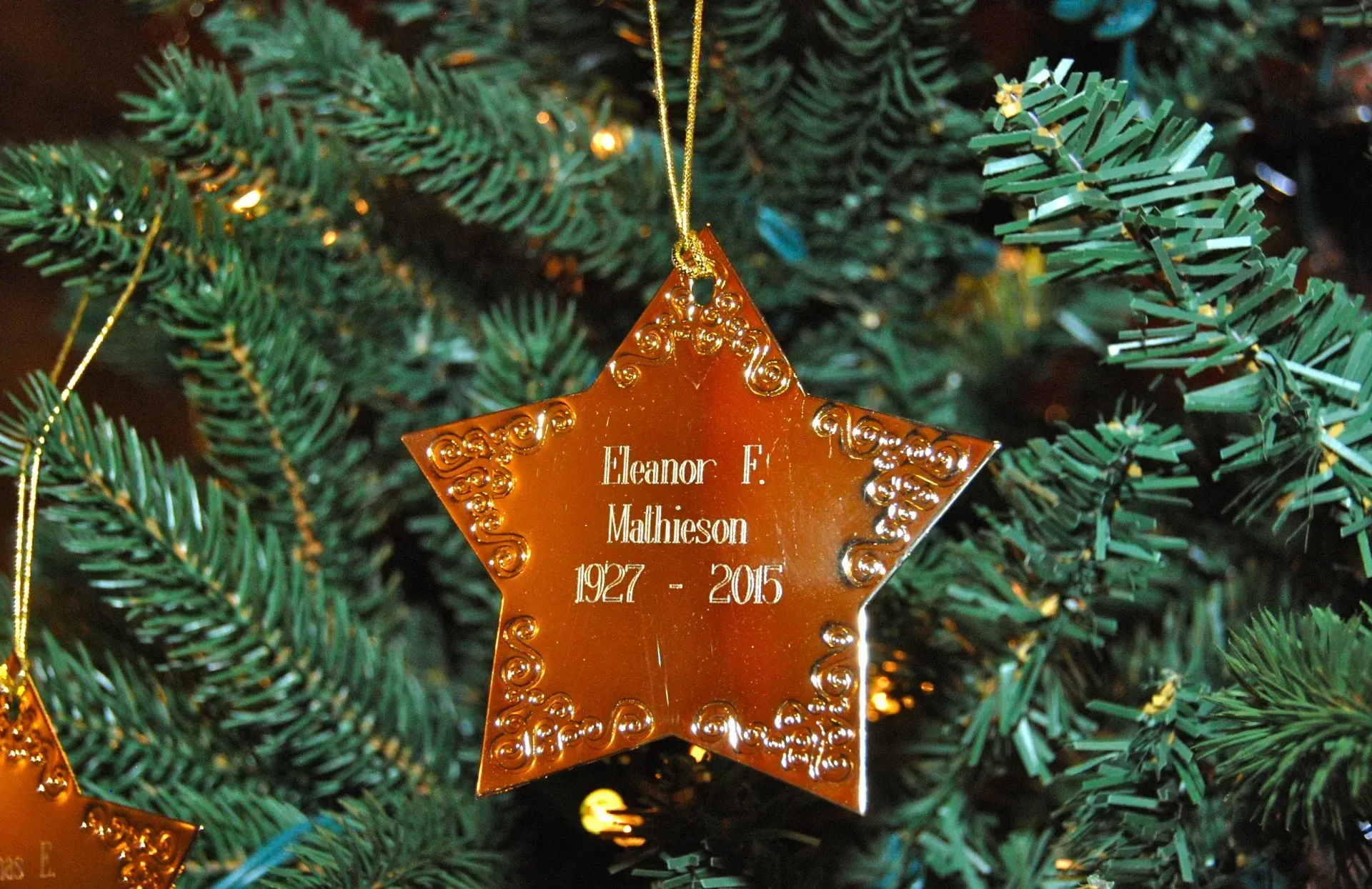 Gold star ornament hanging on a Christmas tree with engraved text.